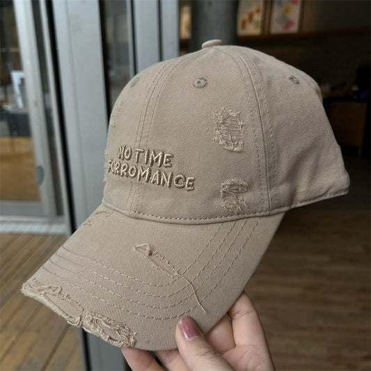 Beige cotton baseball cap with distressed frayed edges and embroidered text on the front panel.
