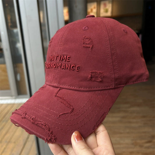 A dark red cotton baseball cap with distressed, frayed edges and embroidered text on the front.
