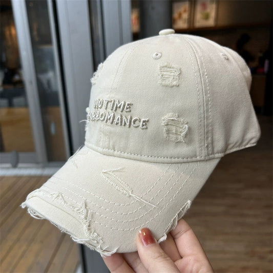 A beige distressed baseball cap with embroidered text, featuring frayed edges and a vintage look.